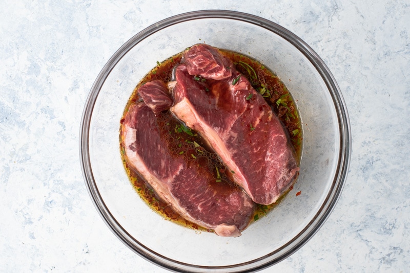 Beef steak marinating in beer in a glass bowl. 