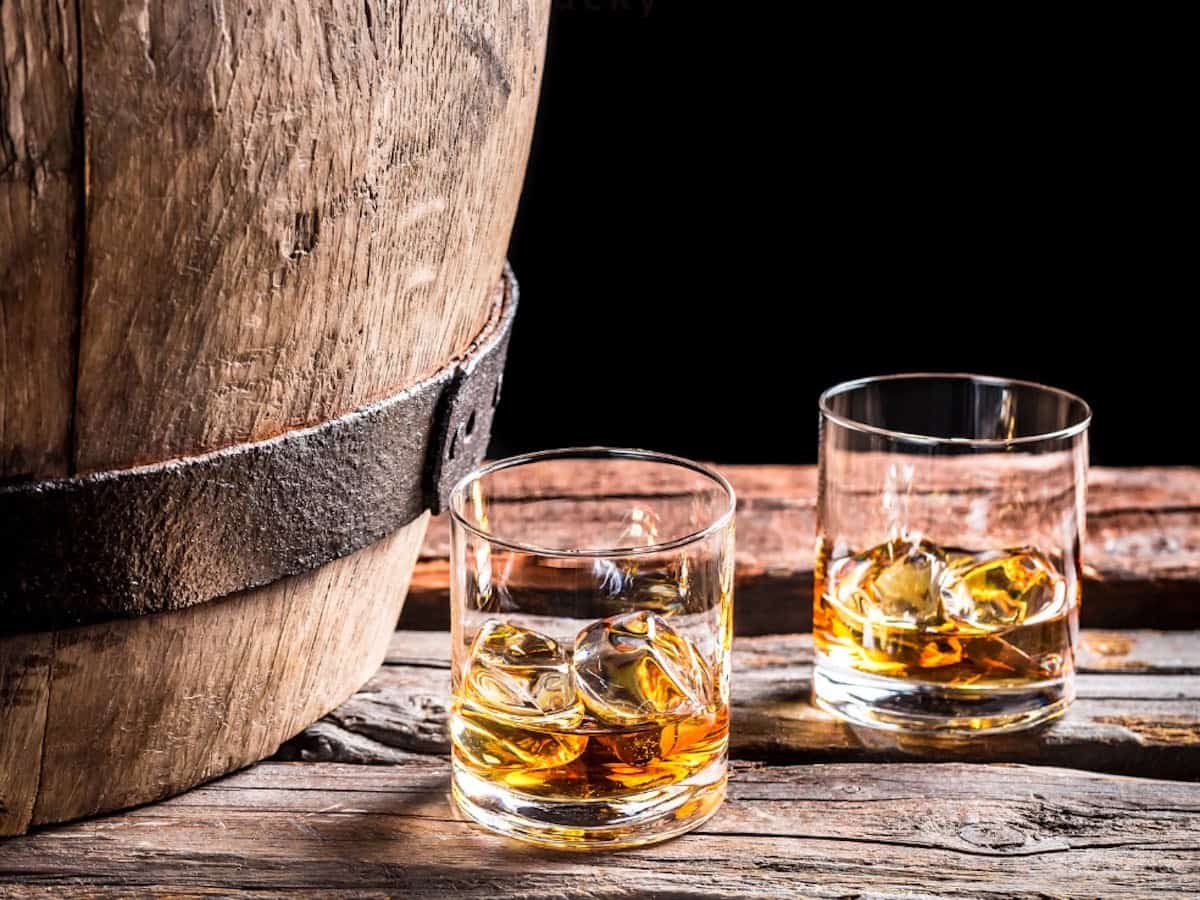 A glass bourbon barrel with two glasses of bourbon.