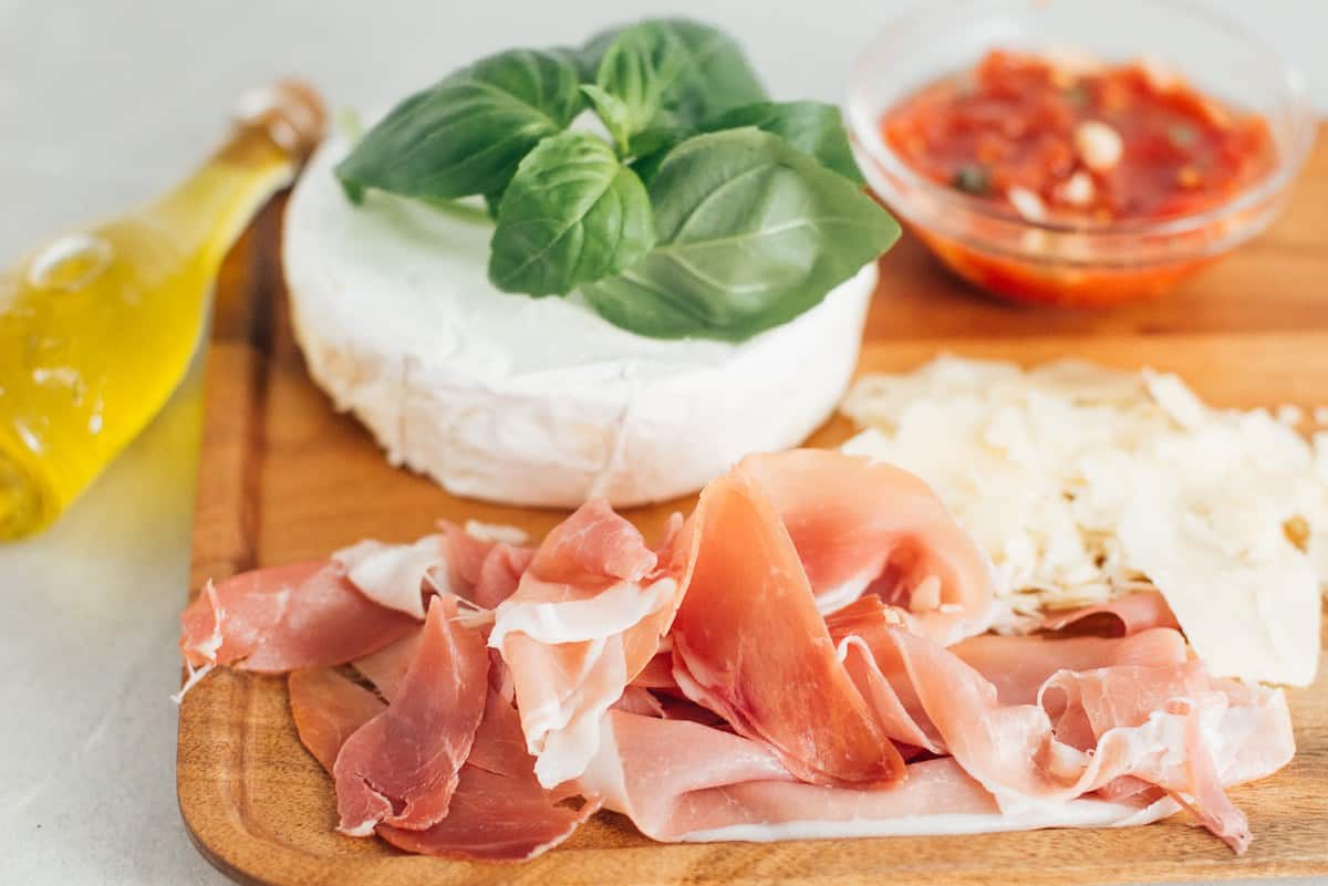 Prosciutto, brie, basil and parmesan toppings for pizza.