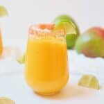 Sparkling mango cocktail with tequila and a background of fresh mangoes.