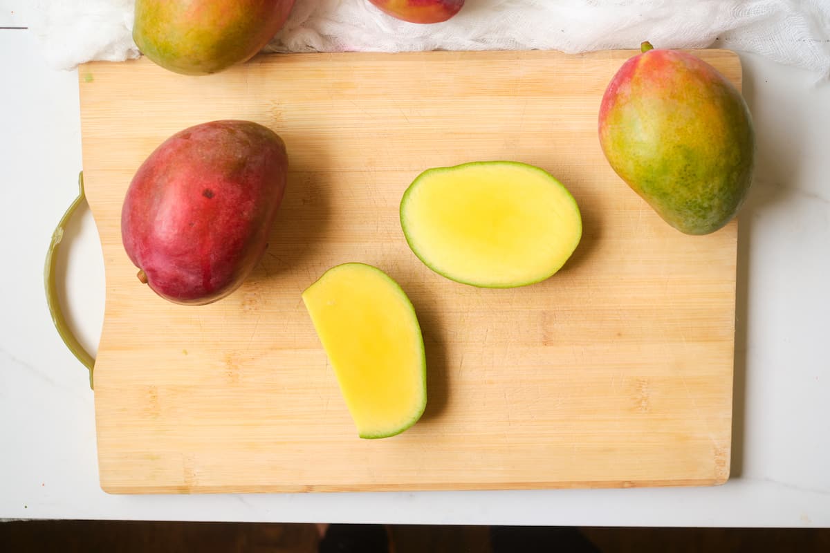 Mango cut in half on a wooden board.