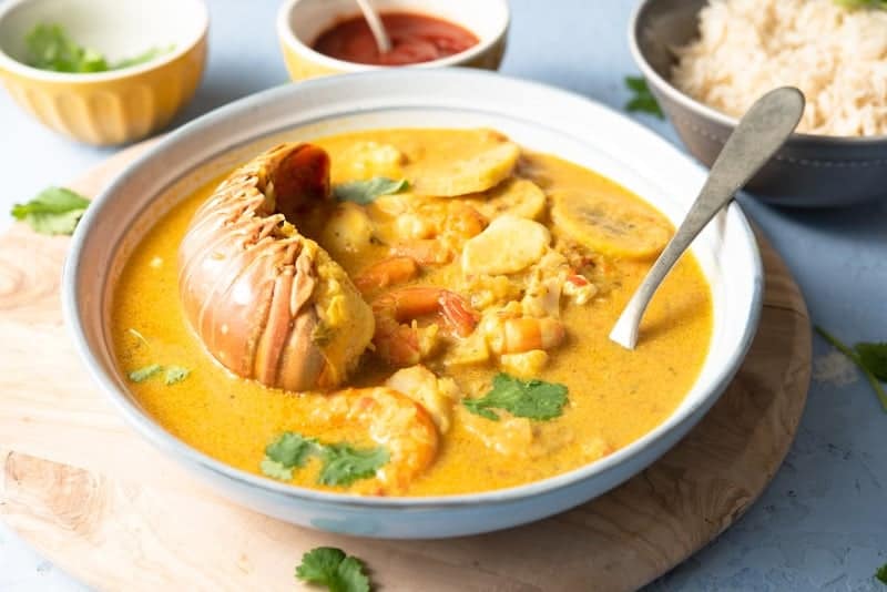 A white bowl of Garifuna tapado seafood soup from Guatemala with rice on the side. .