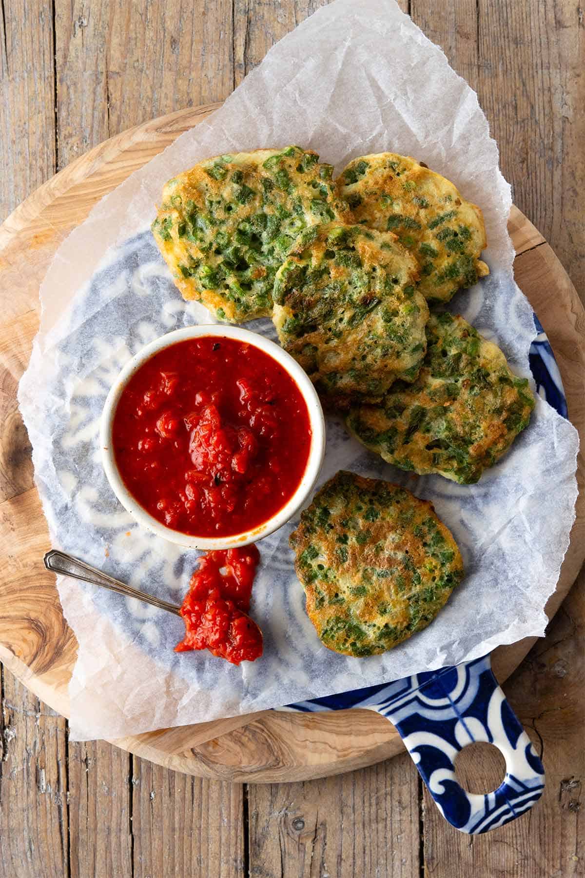 Portrait of tortitas de ejote served with spicy tomato salsa in a bowl on a wooden board. 