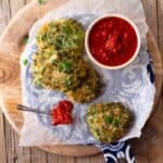 Ejotes fritters on a platter topped with parchment paper and sauce.