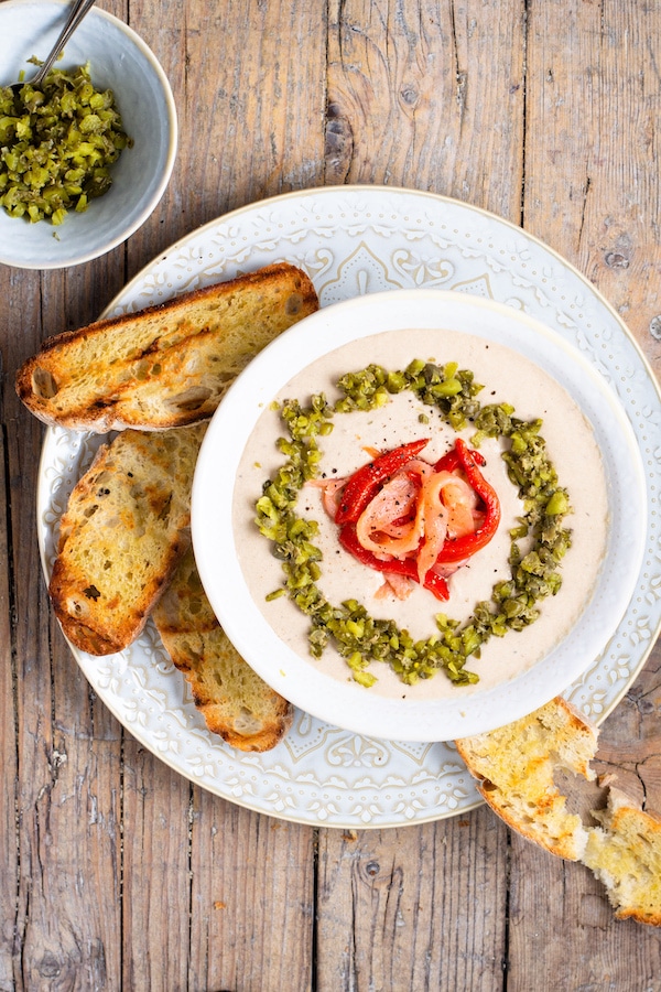 A white bowl with cream of canned sardines surrounded by toast.