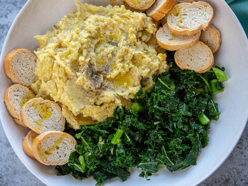 Pure di fave and Cicorie with crostini on a white plate.