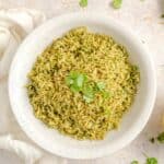 Green rice in a white bowl topped with fresh cilantro leaves.