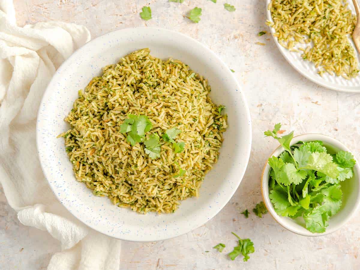 A bowl of arroz verde on the table with cilantro leaves.