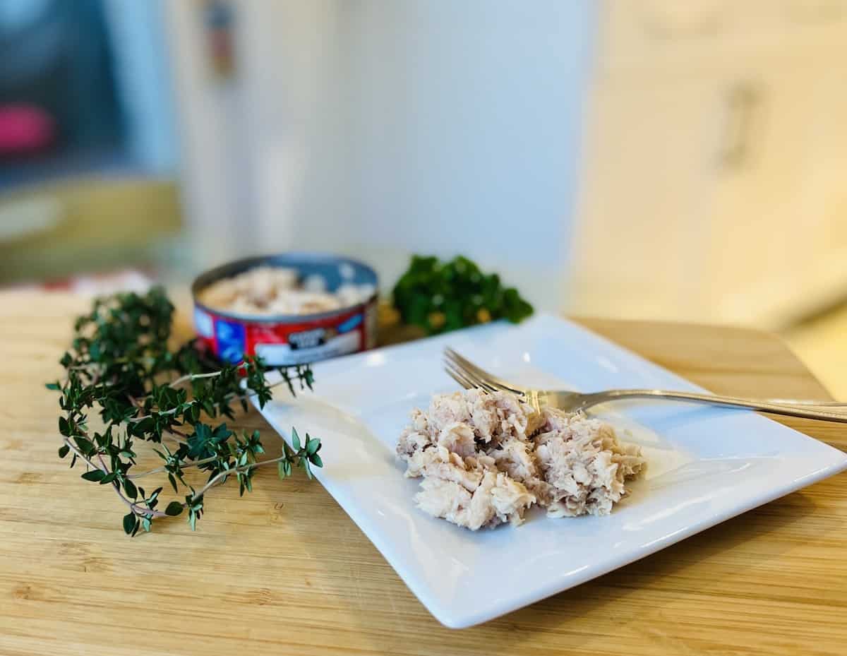 A can of salmon on a white plate with thyme and parsley.