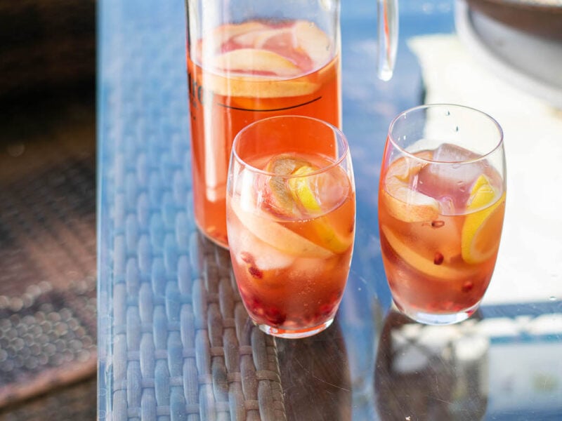 Bourbon punch pitcher and glasses with ices on patio table.