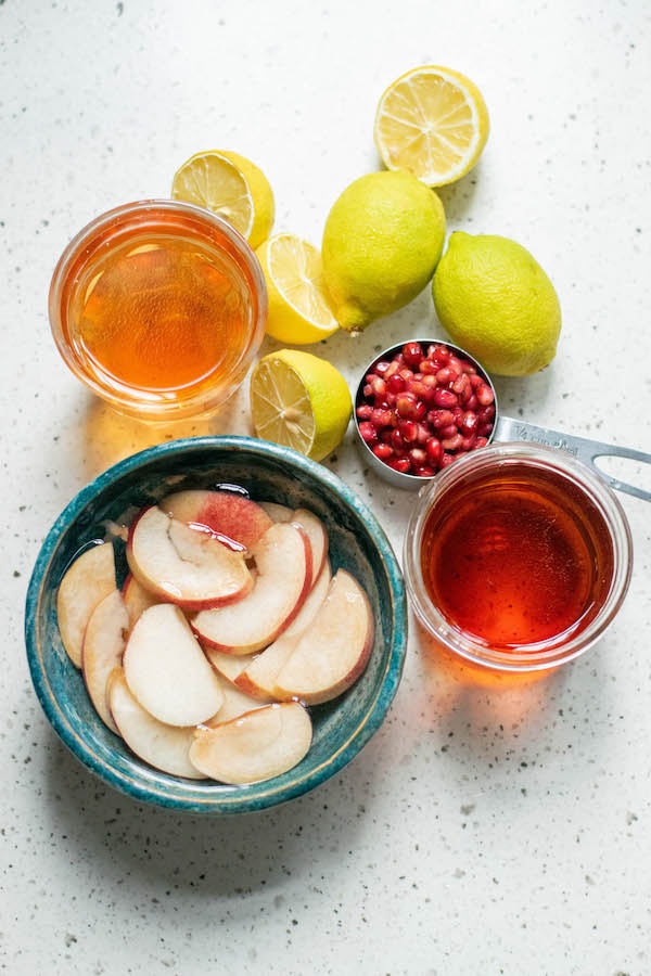 Ingredients for bourbon peach punch including pomegranate seeds, lemon, bourbon and fresh peaches. 