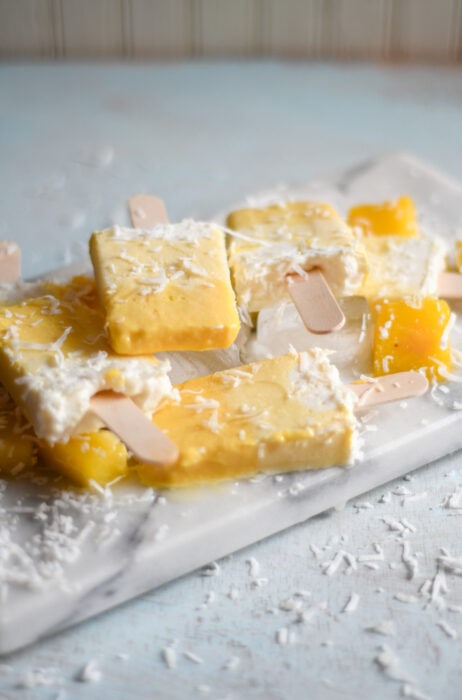 Non-alcoholic Pina Colada Ice Pops on a marble serving tray. 