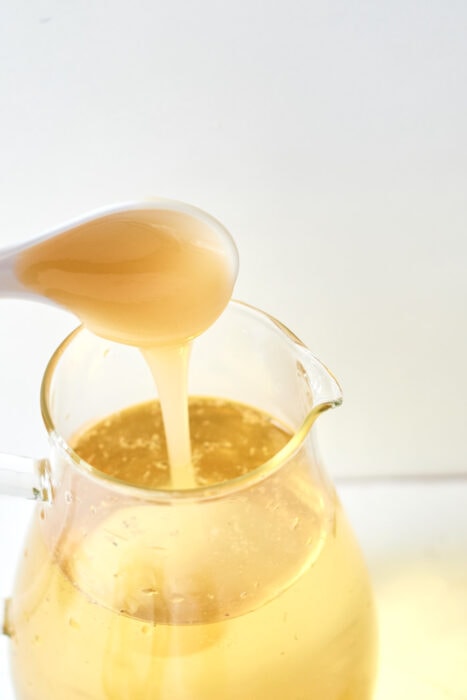 a spoonful of honey being poured into a pitched of iced chamomile tea