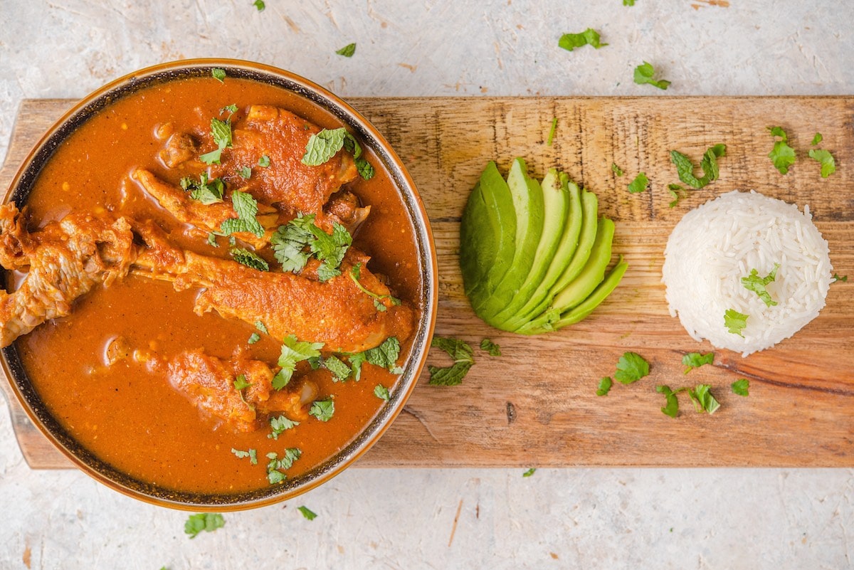 Guatemalan kakik de pavo on a wooden board with white rice and sliced avocado.
