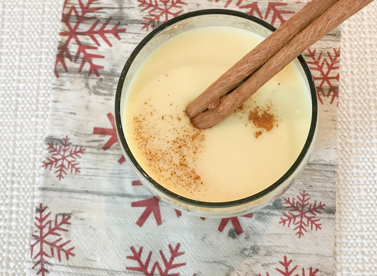 Glass of eggnog on a napkin with a cinnamon stick.