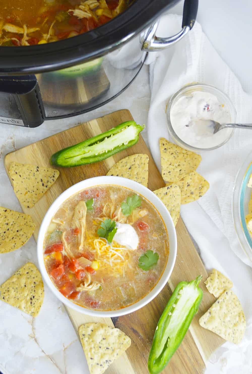 Overhead shot of chicken chipotle soup with a slow cooker in background. 