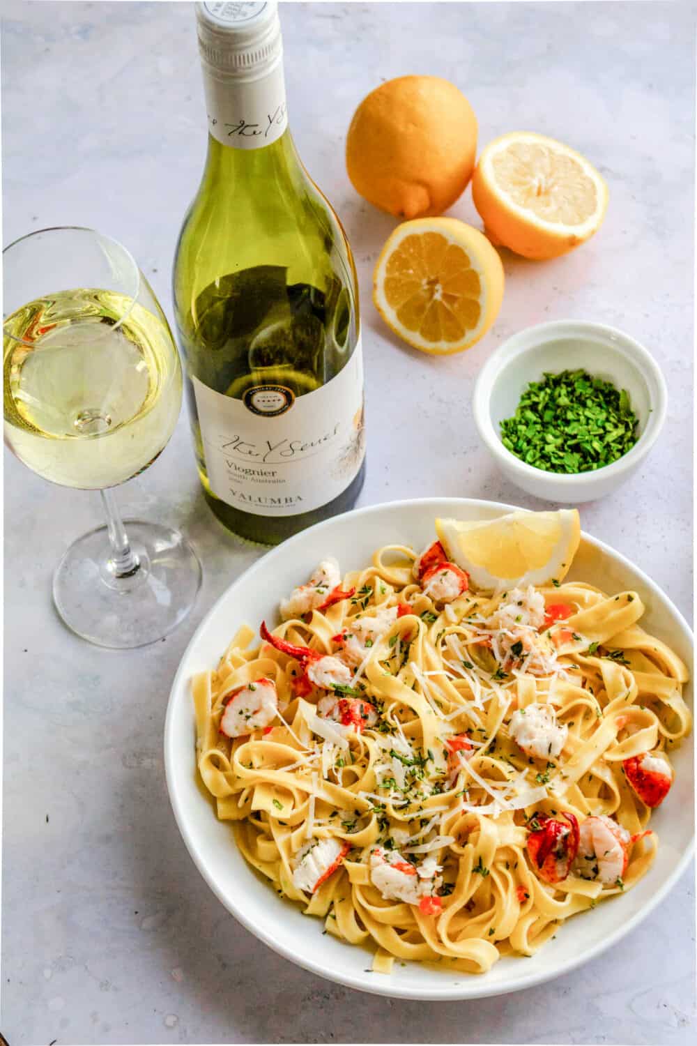 Lobster fettuccine in a bowl with a bottle of vigonier wine and wine glass. past