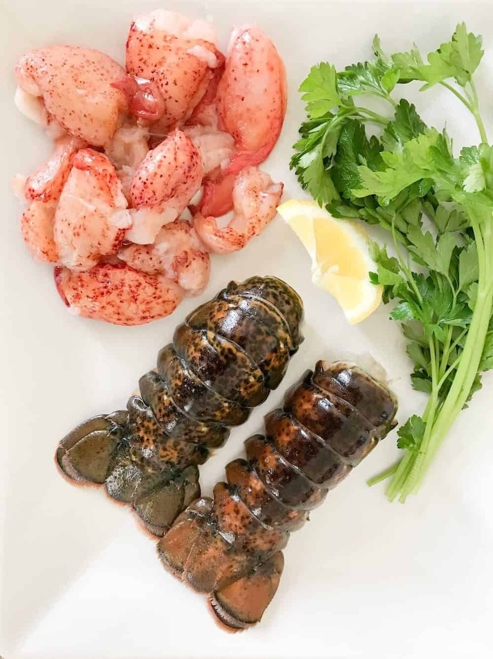 Lobster tails and lobster meat with parsley and lemon on a white plate.