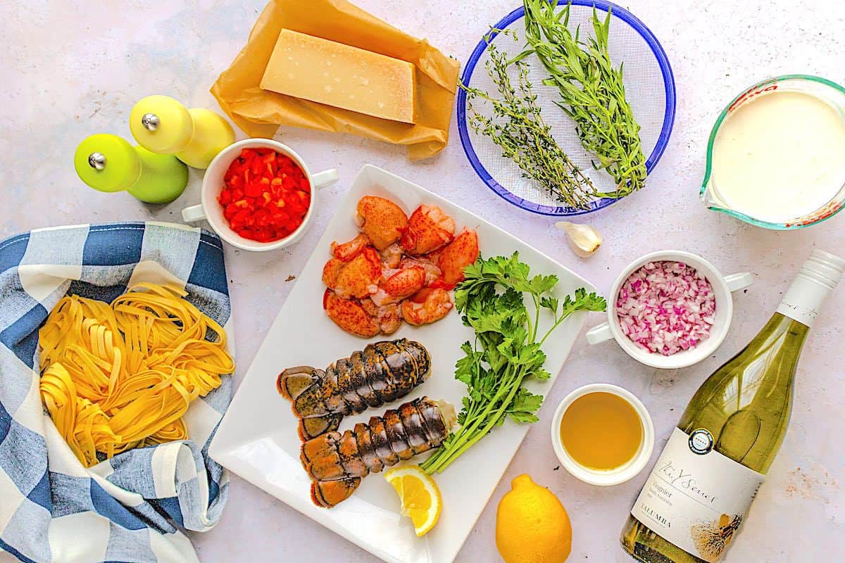 Overhead shot of ingredients for lobster pasta recipe include fresh herbs, lobster, red onion, garlic fettuccine, sweet red pepper, Yalumba Y Series viognier wine, lemon zest, heavy cream, parmesan and olive oil. 