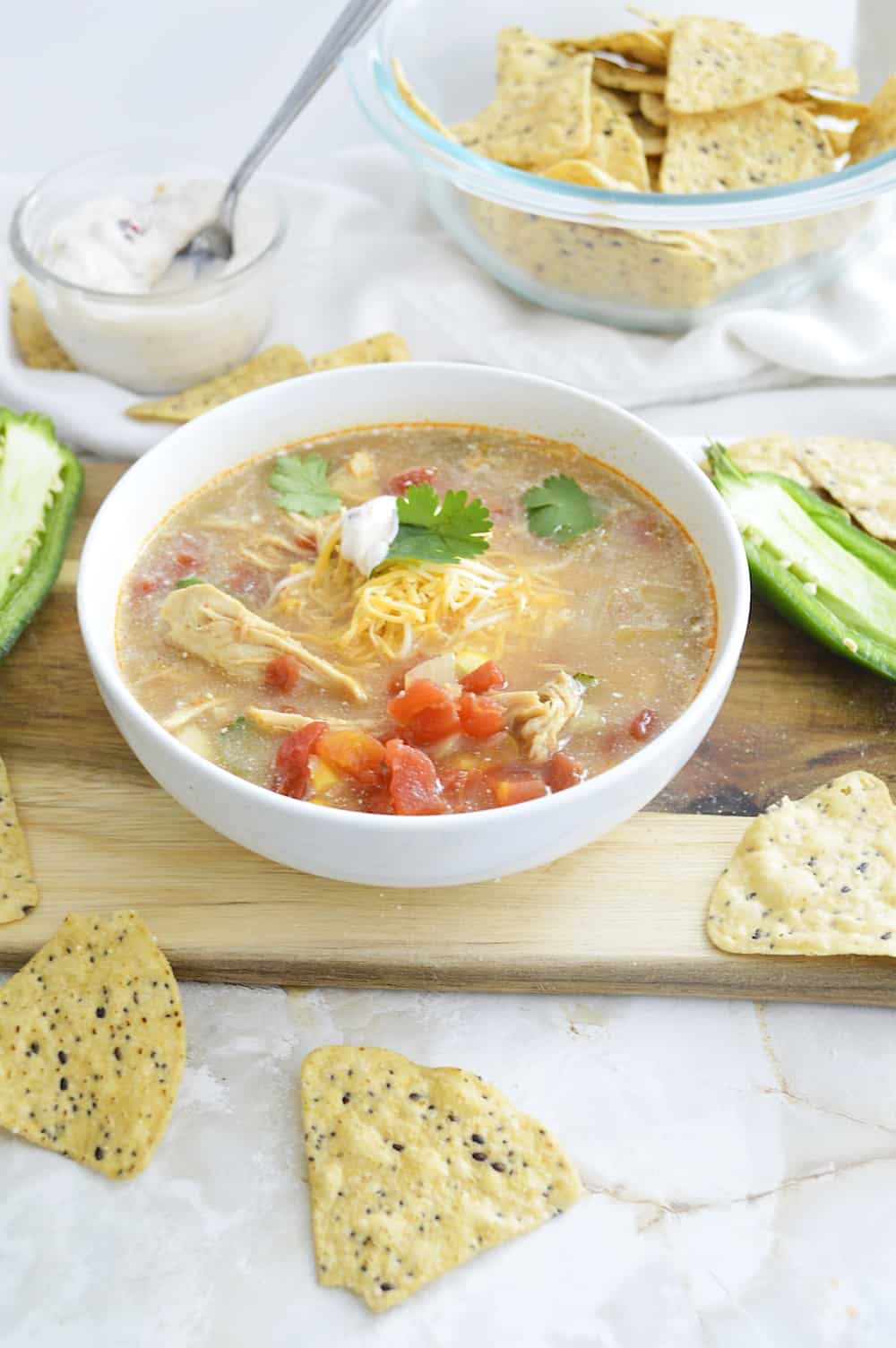 White bowl of crock pot chicken tortilla stew on a wooden board.