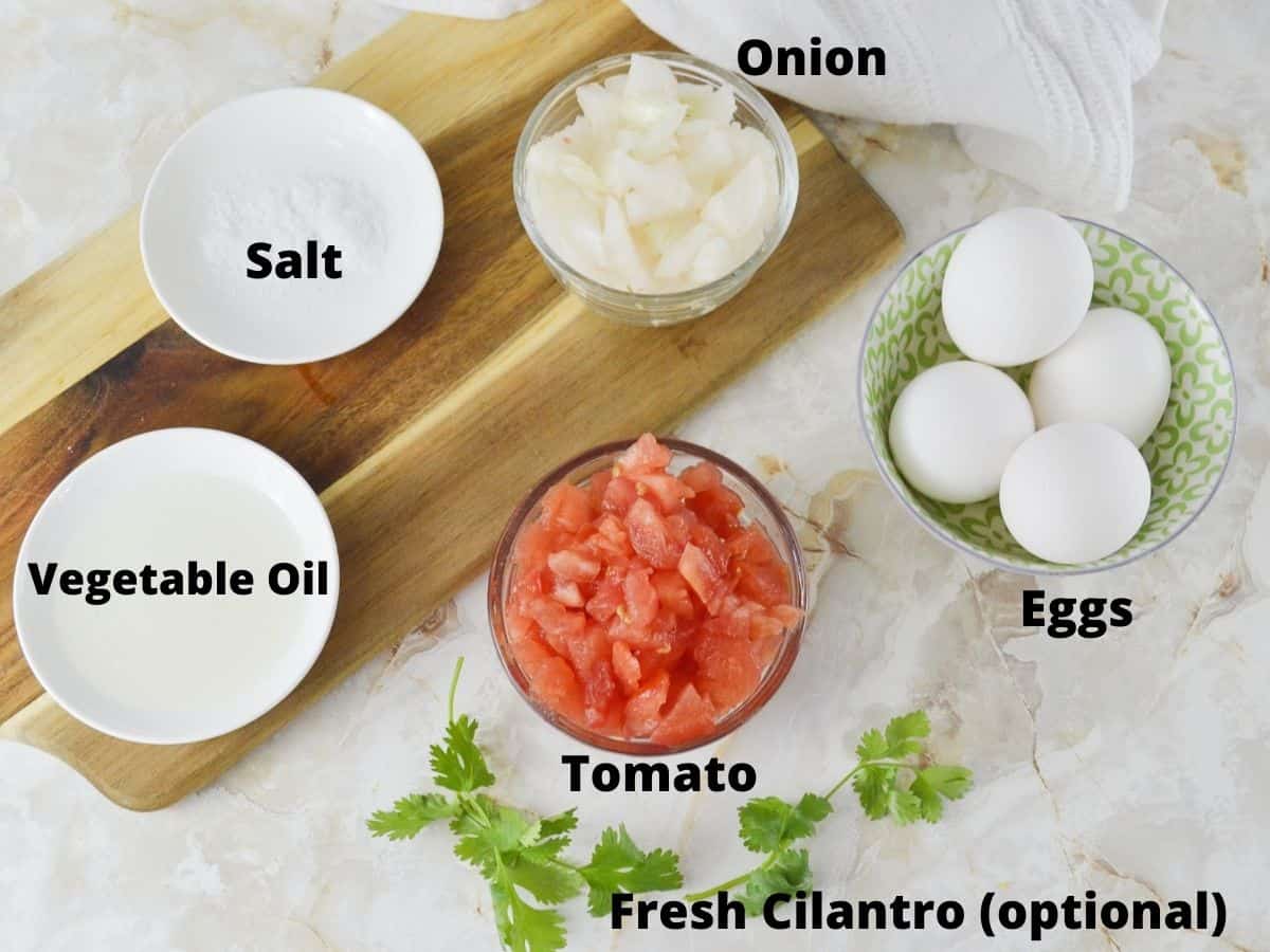 Ingredeints for scrambled eggs with tomato and onion including vegetable oil and salt.
