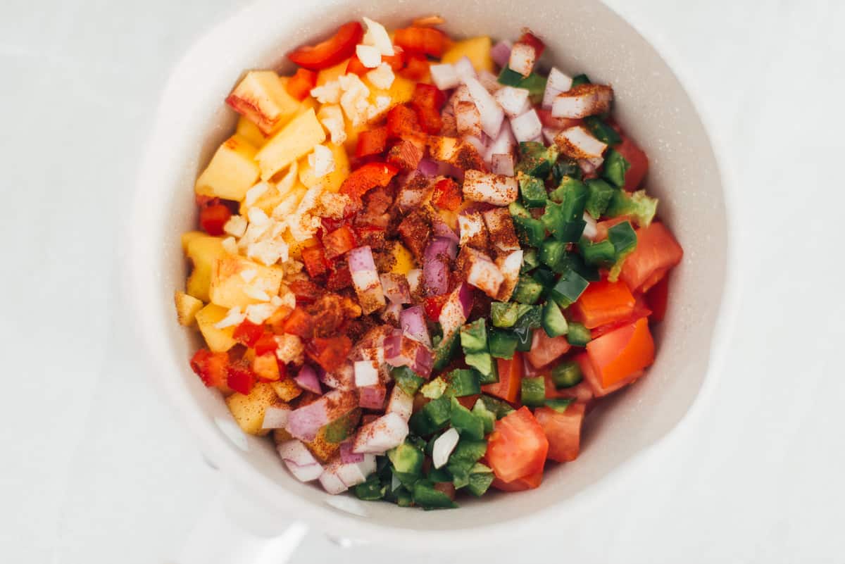 Cumin and chipotle spices with peaches, tomato and pepper in a pot.