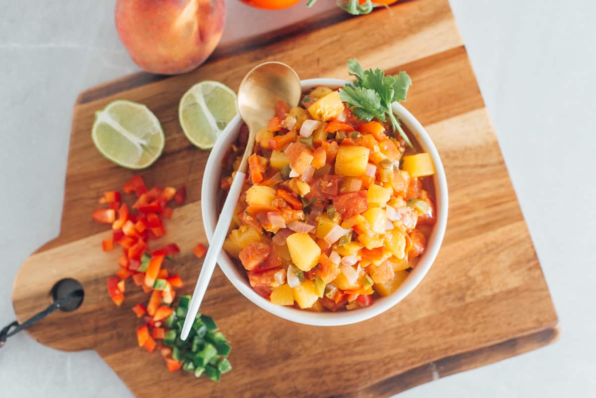 Fresh peach salsa in a bowl on a cutting board.