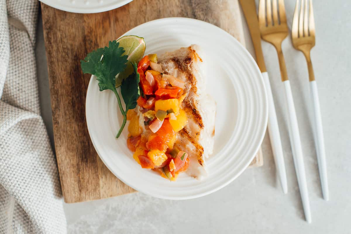 Overhead shot of grilled fish with peach sauce with cutlery..