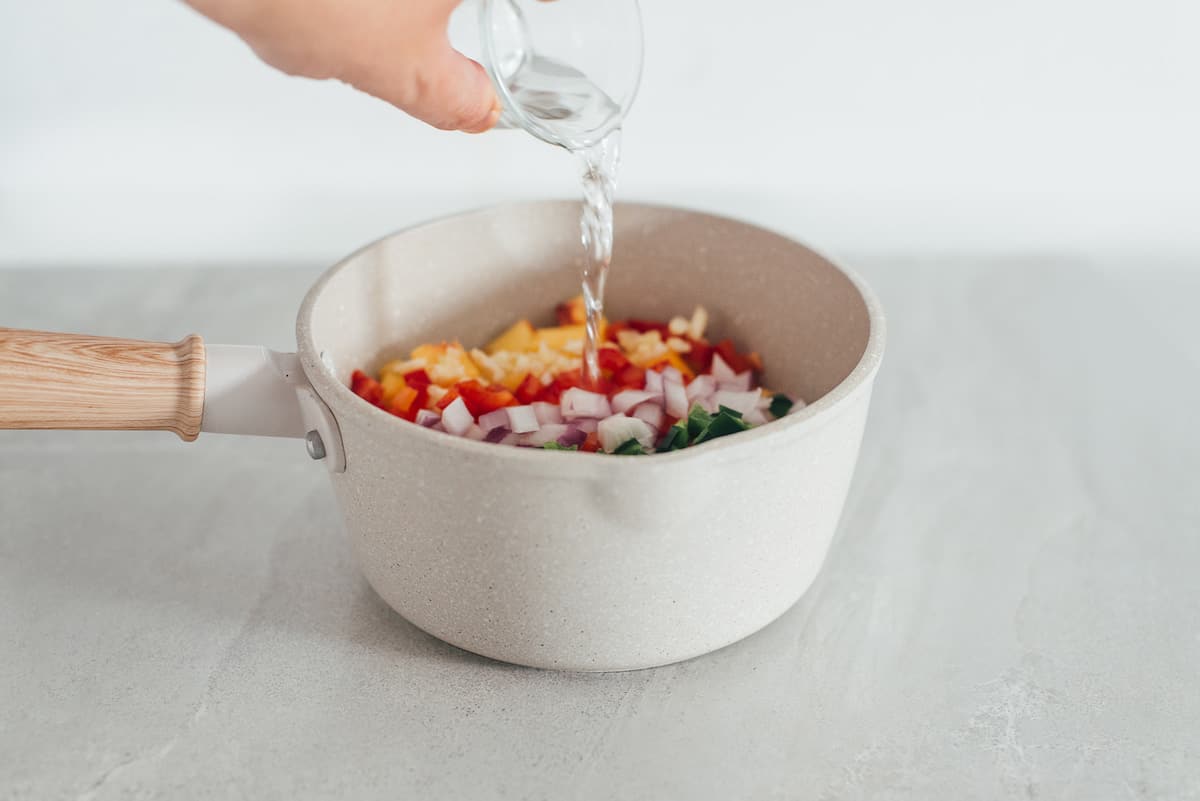 Pouring vinegar into a cooking pot to make peach salsa.