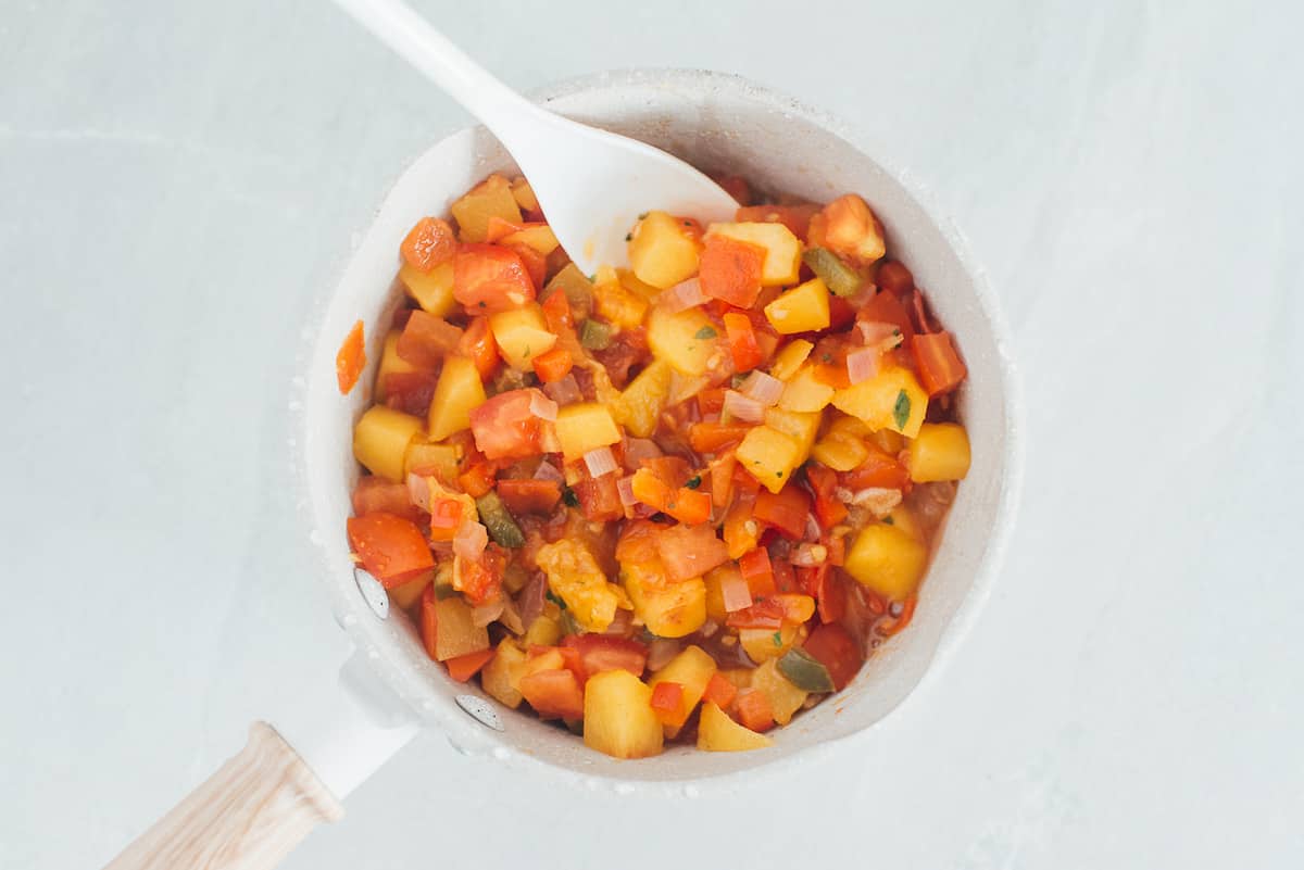 Spoon in a pot of peach sauce as it cooks.