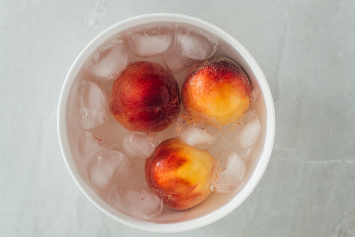 Blanching peaches for salsa in ice in a white bowl. 