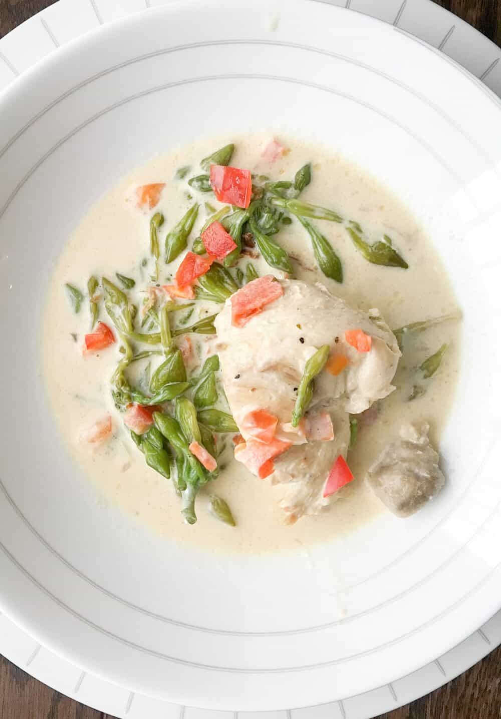 Chicken with loroco in cream sauce in a white bowl.