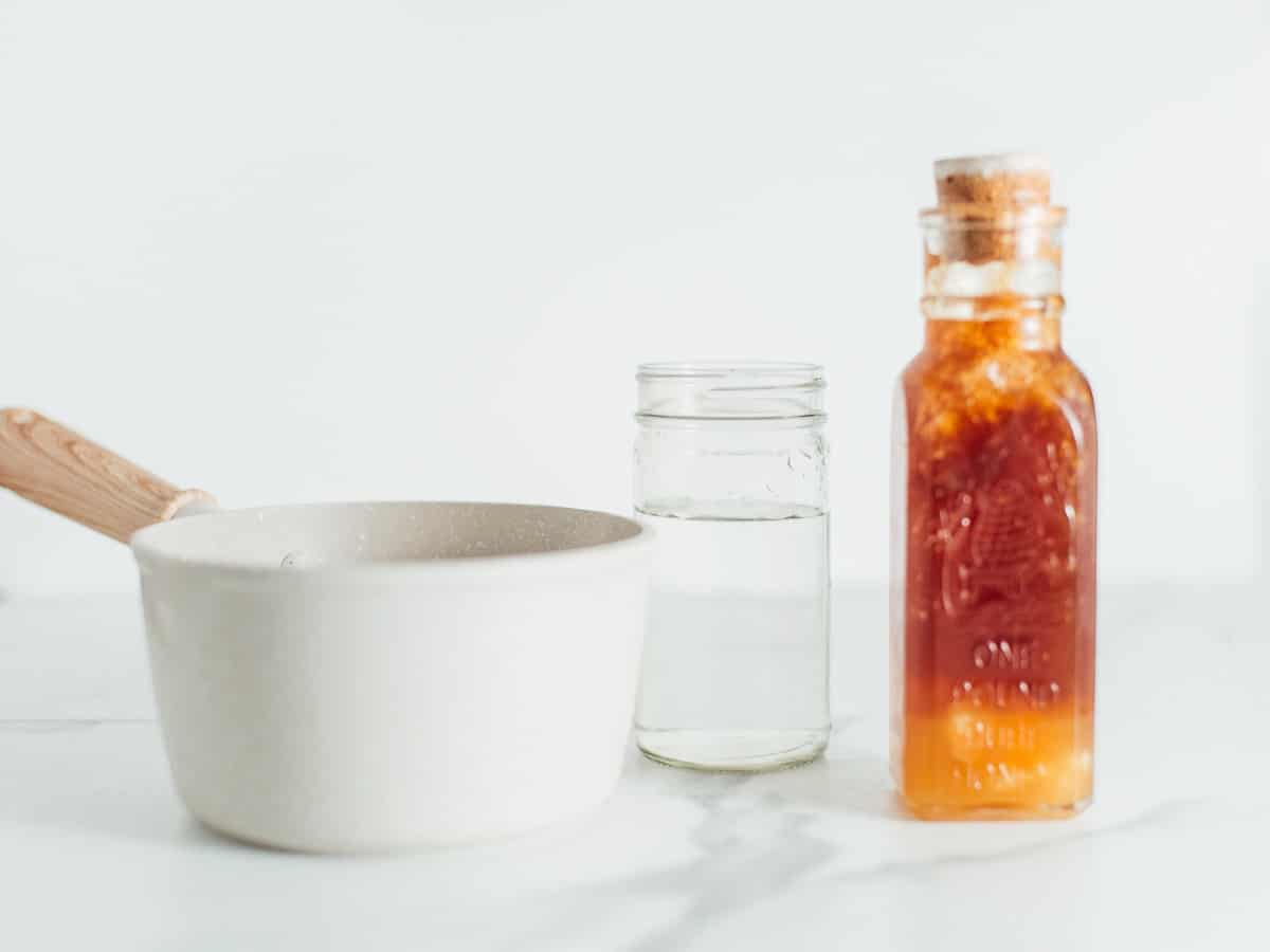 a small white ceramic pot, a clear jar with liquid, a stoppered jar with amber liquid