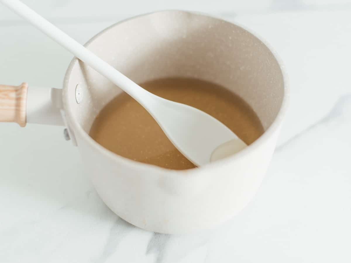 a small white ceramic pot with honey simple syrup on the bottom and a white spoon resting inside