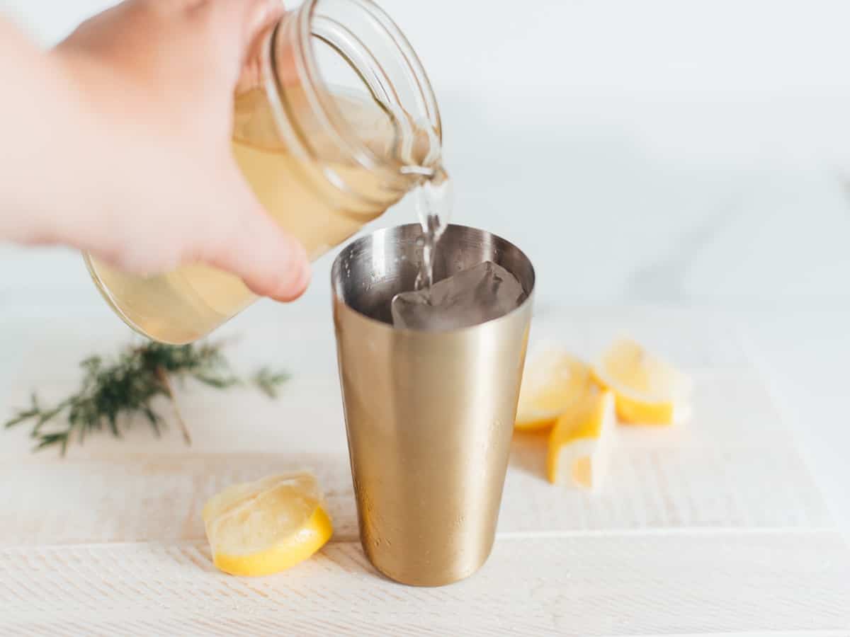 pouring liquid from a jar into a drink shaker filled with ice