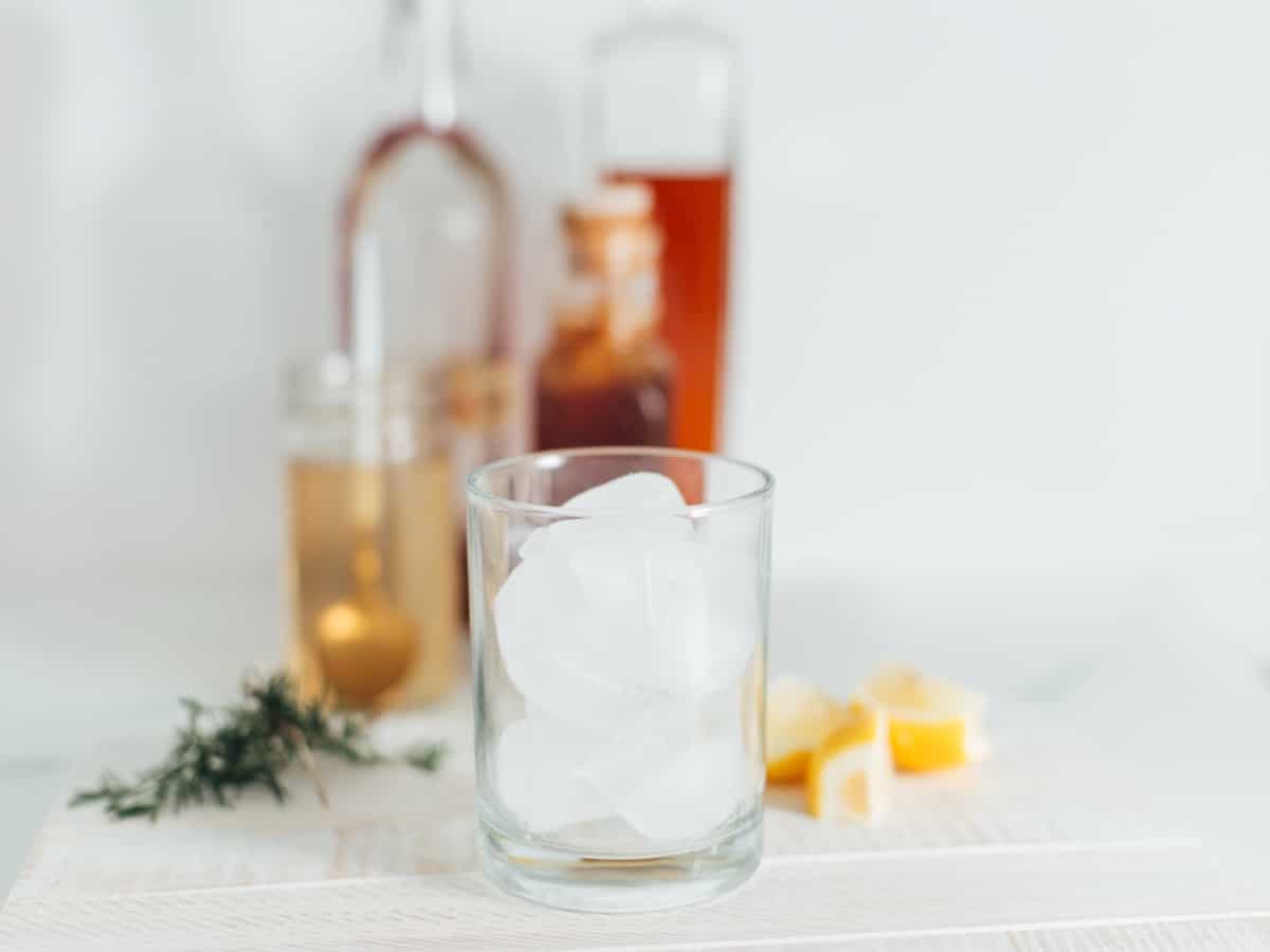 a highball glass filled with ice with lemon, rosemary, honey syrup in the background to make a chamomile whiskey cocktail