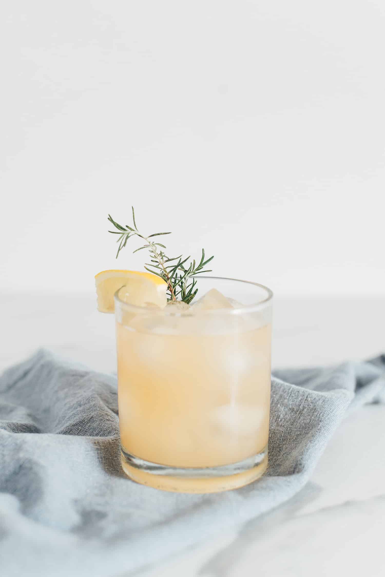 Portrait of a chamomile drink with a sprig or rosemary and fresh lemon on a pale blue napkin. 