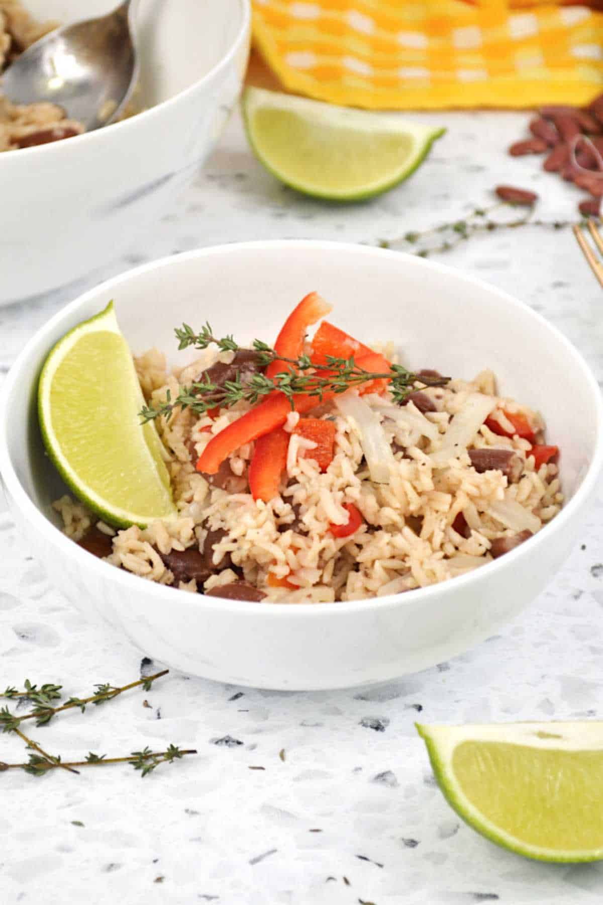 Guatemalan coconut rice and beans in a bowl garnished with lime, fresh thyme and red pepper.