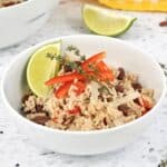 A bowl of coconut red beans and rice on the counter with a lime and bell pepper.