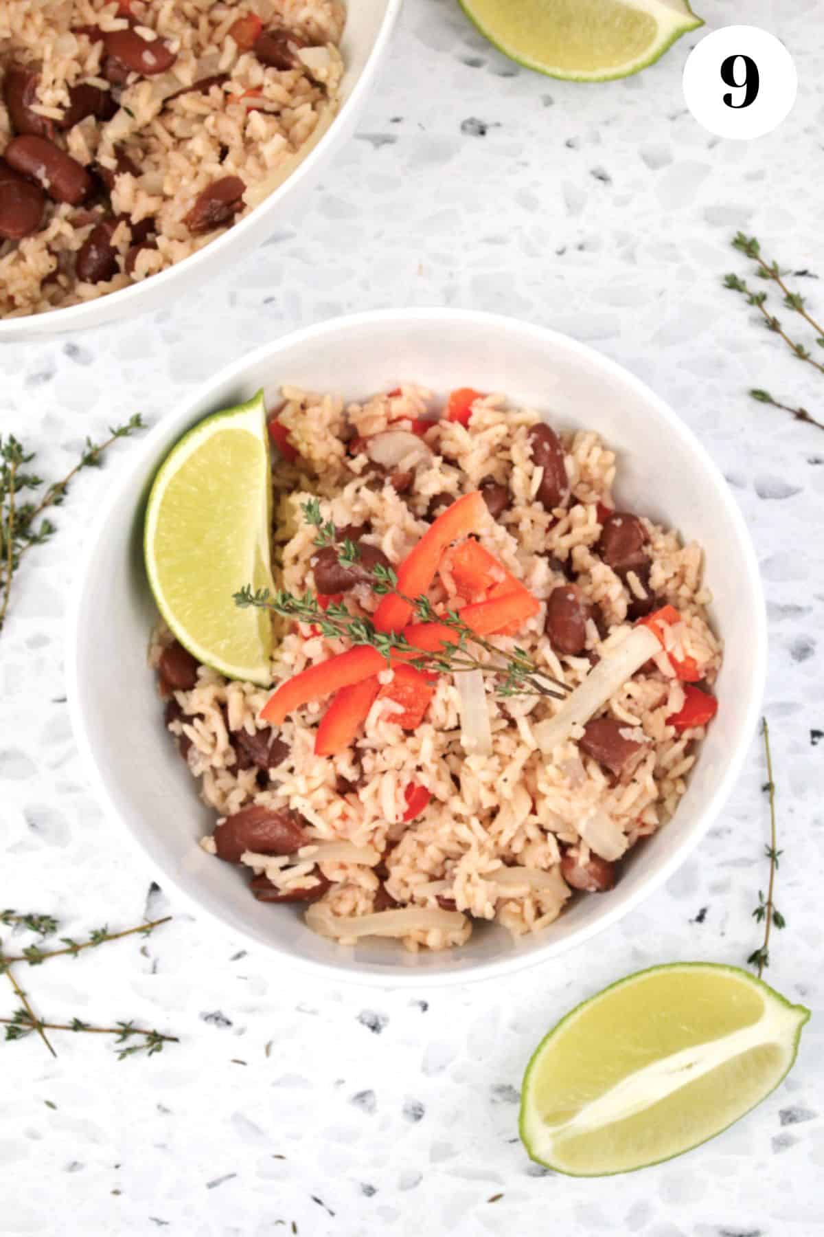 A bowl of coconut rice and beans garnished with lime wedges and red peppers.