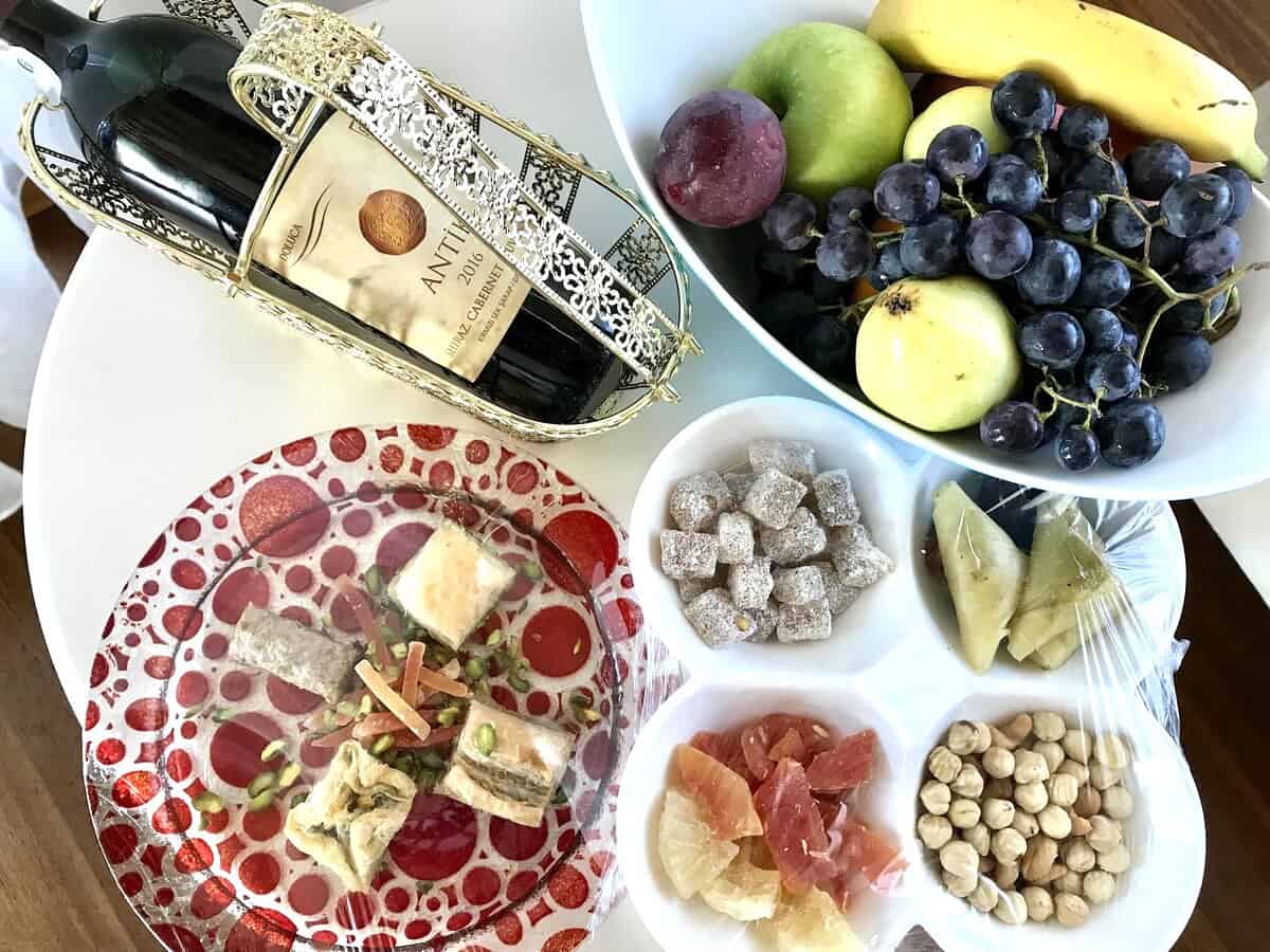 A bottle of Doluca wine with Turkish Delight, fruit and nuts on a serving tray.