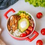A healthy chipotle bowl on the table with cherry tomatoes and lettuce around it.