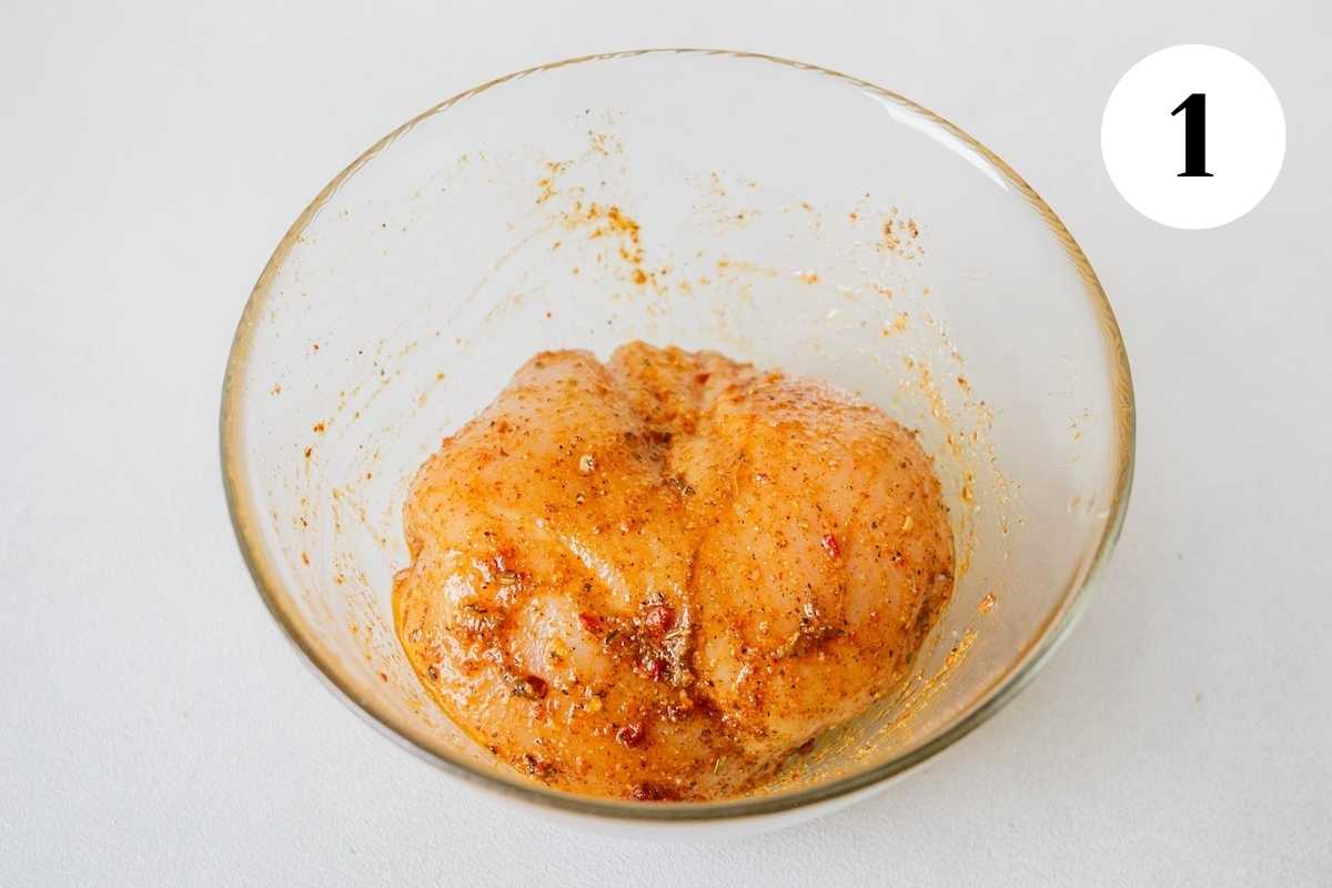 Chicken marinating in chipotle spice seasoning in a glass bowl.