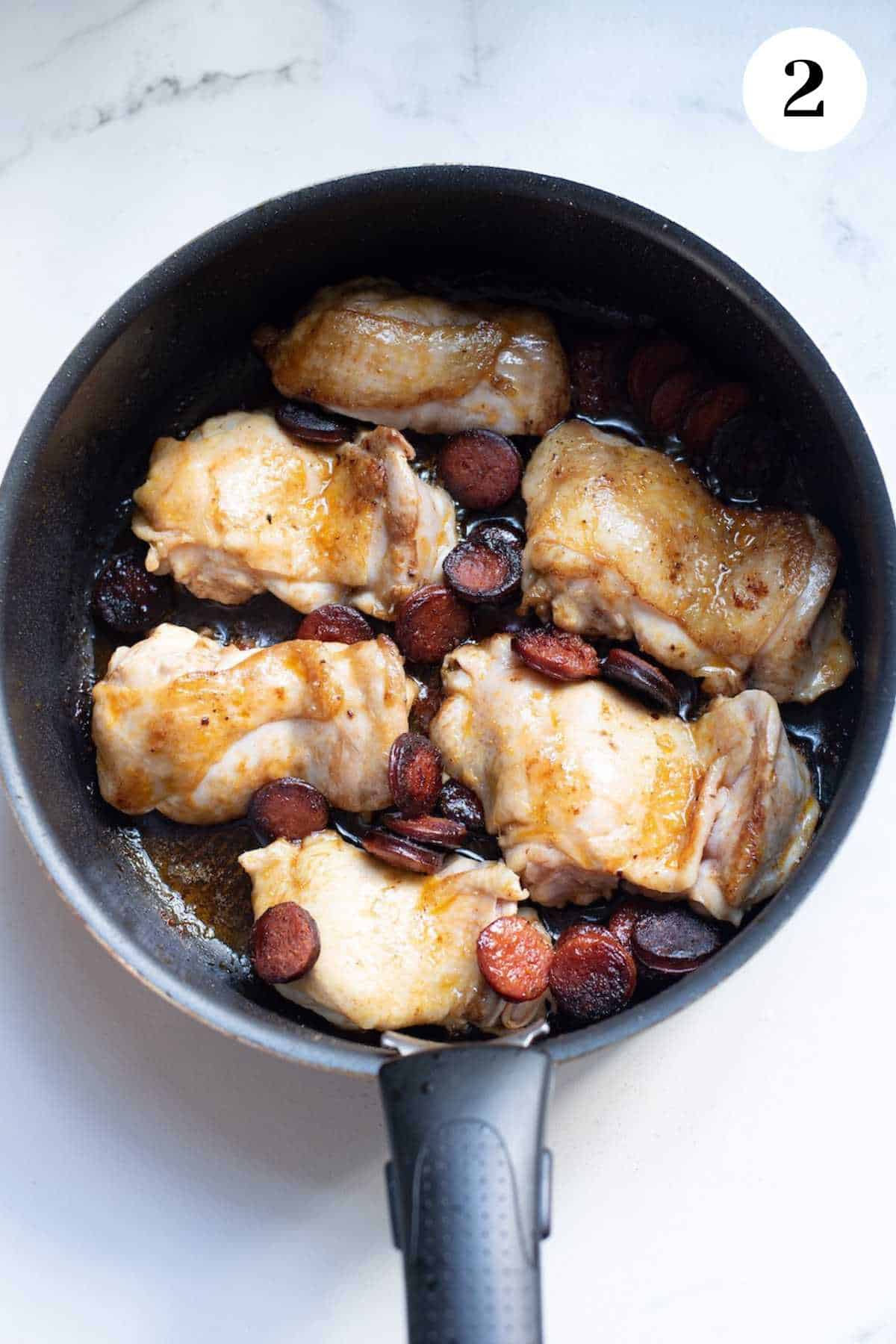 Chicken browning in a cast iron skillet.