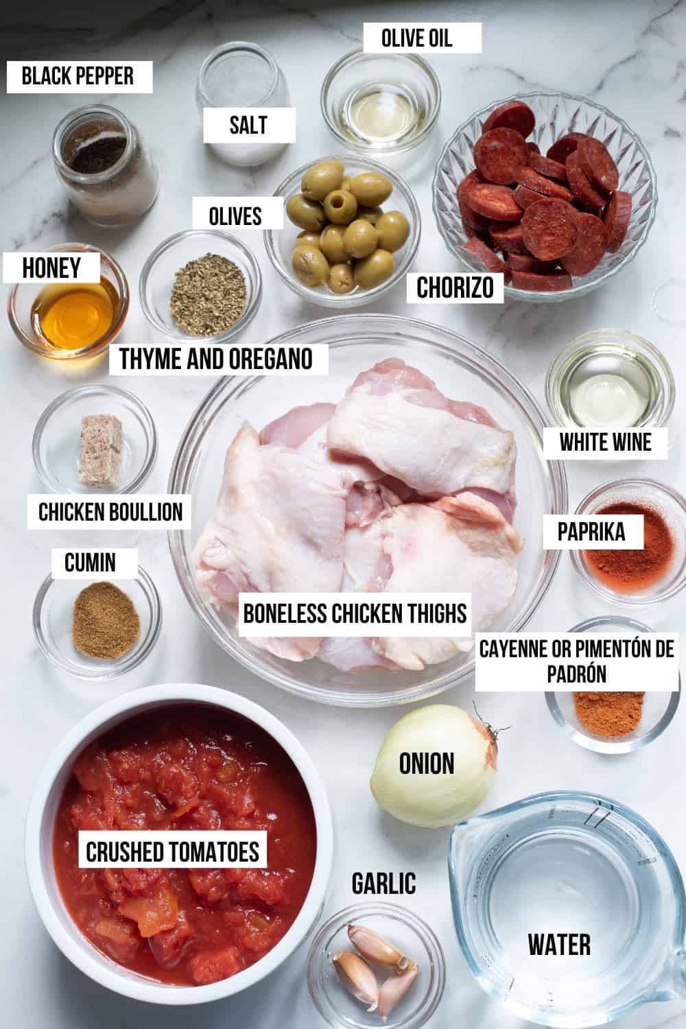 Labelled ingredients for Spanish stew chicken including boneless chicken, white wine, garlic, onion, crushed tomatoes, spices, olive oil, olives, honey, boullion and chorizo.