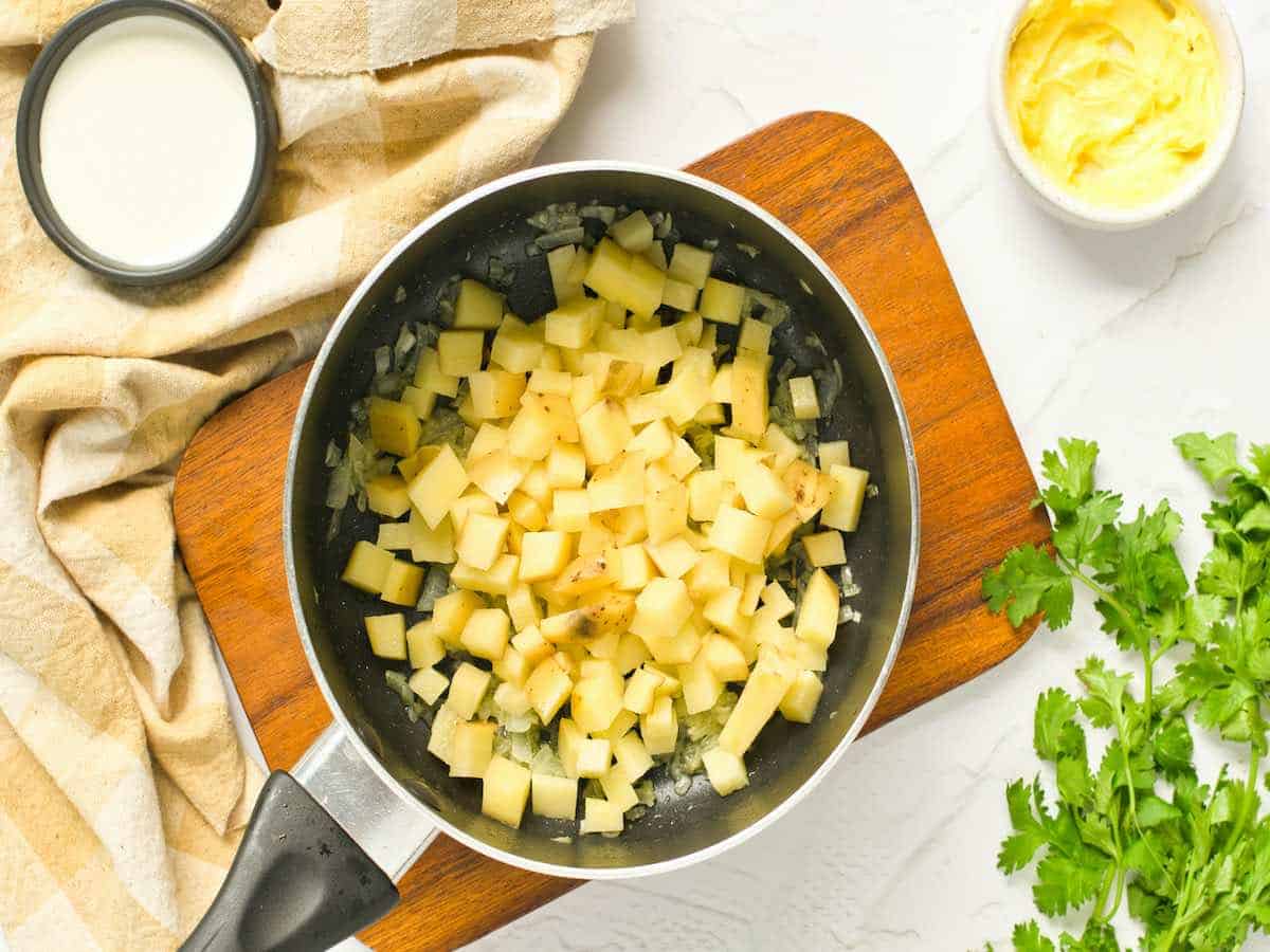 Chopped potatoes in a pan with butter to make potato soup.