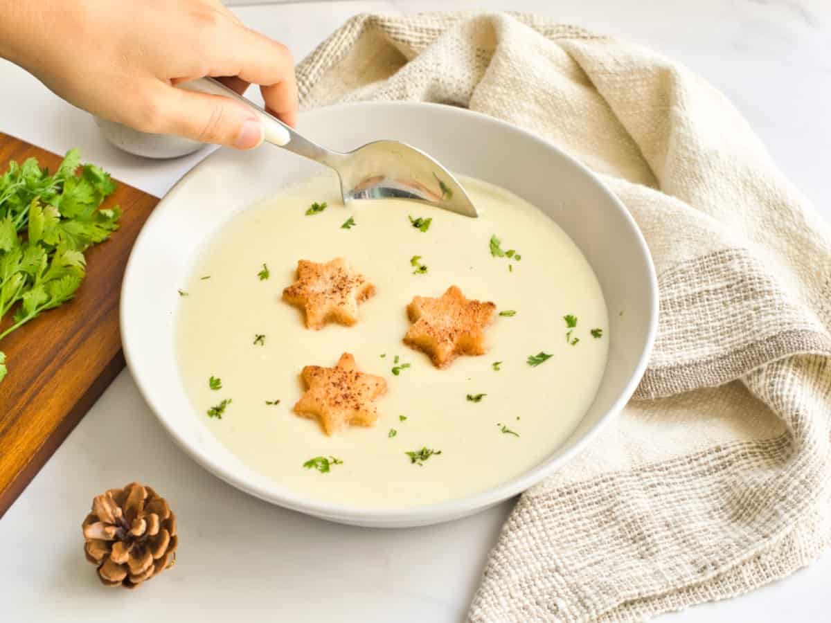 A woman's hand holding a spoon in a bowl of holiday potato soup. 