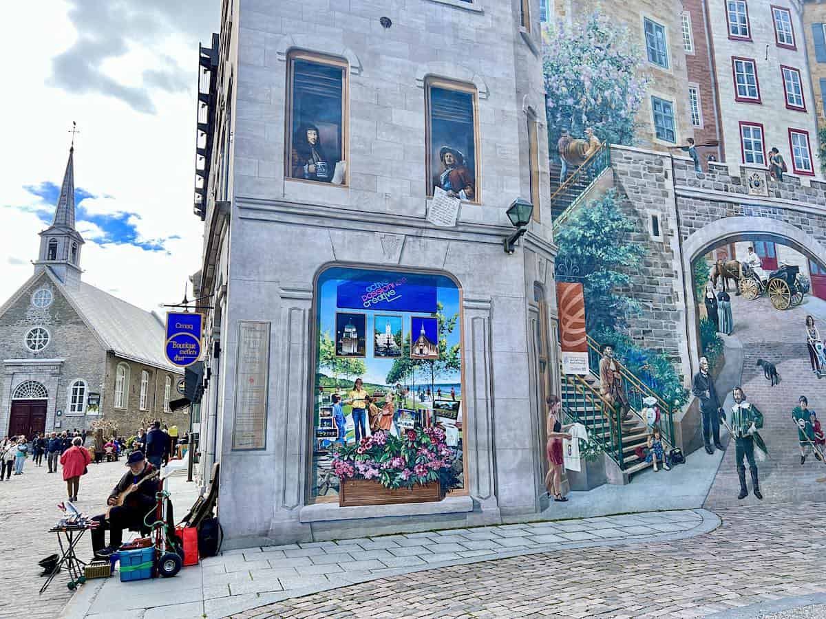A street musician beside a fresco in Quebec City.  