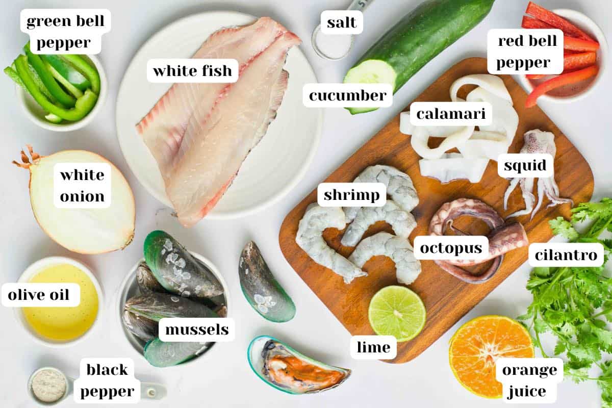 White onion, mussels, olive oil, black pepper, salt, shrimp, octopus, squid, calamari, red and green bell pepper, orange juice, fresh lime and cilantro on a wooden board.