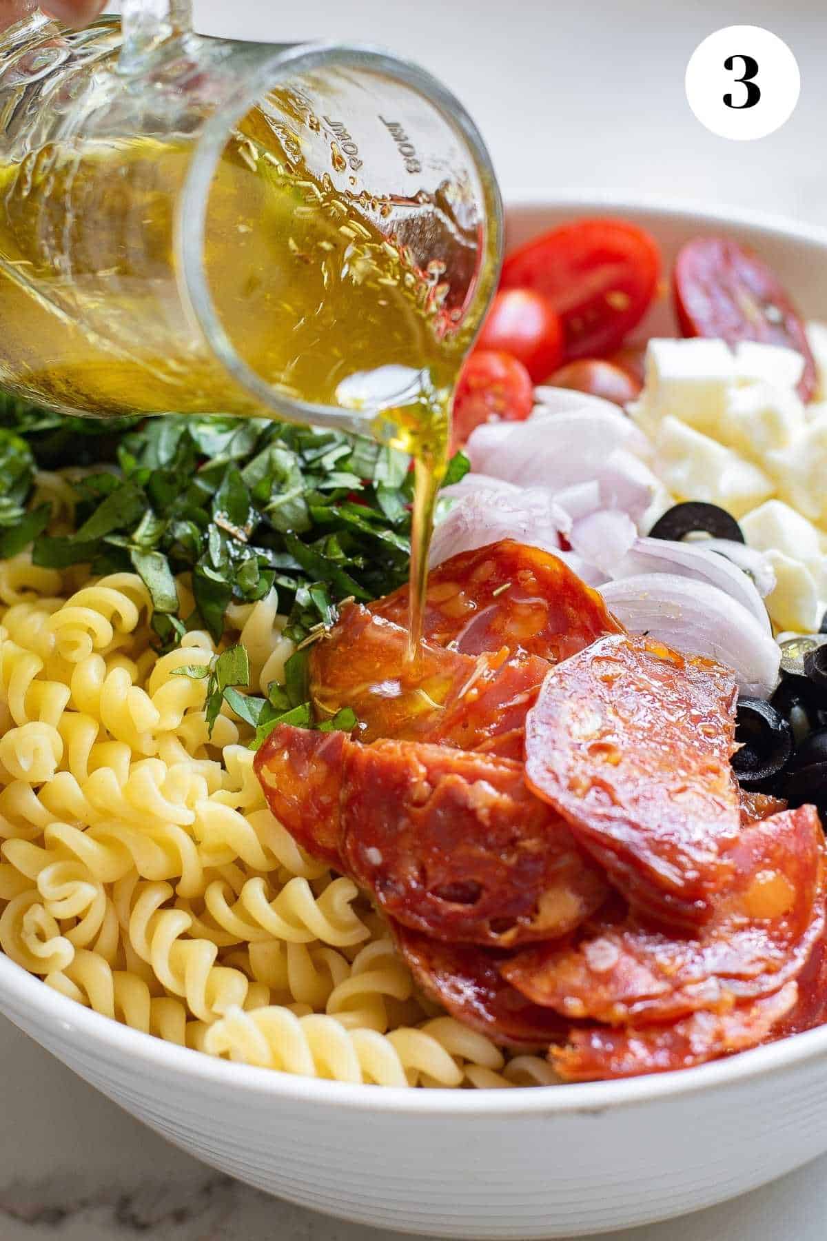 Pouring the dressing over the bowl of pizza pasta salad.